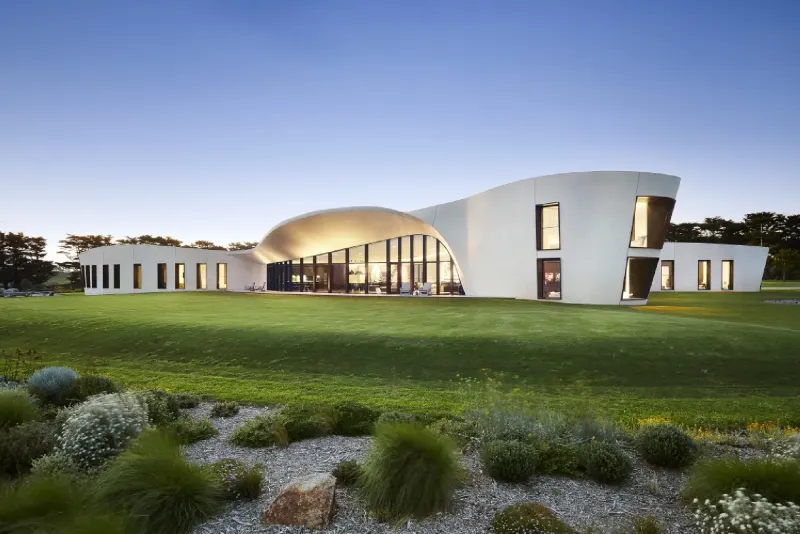 Contemporary curved white residence at dusk set in landscaped lawn and native planting