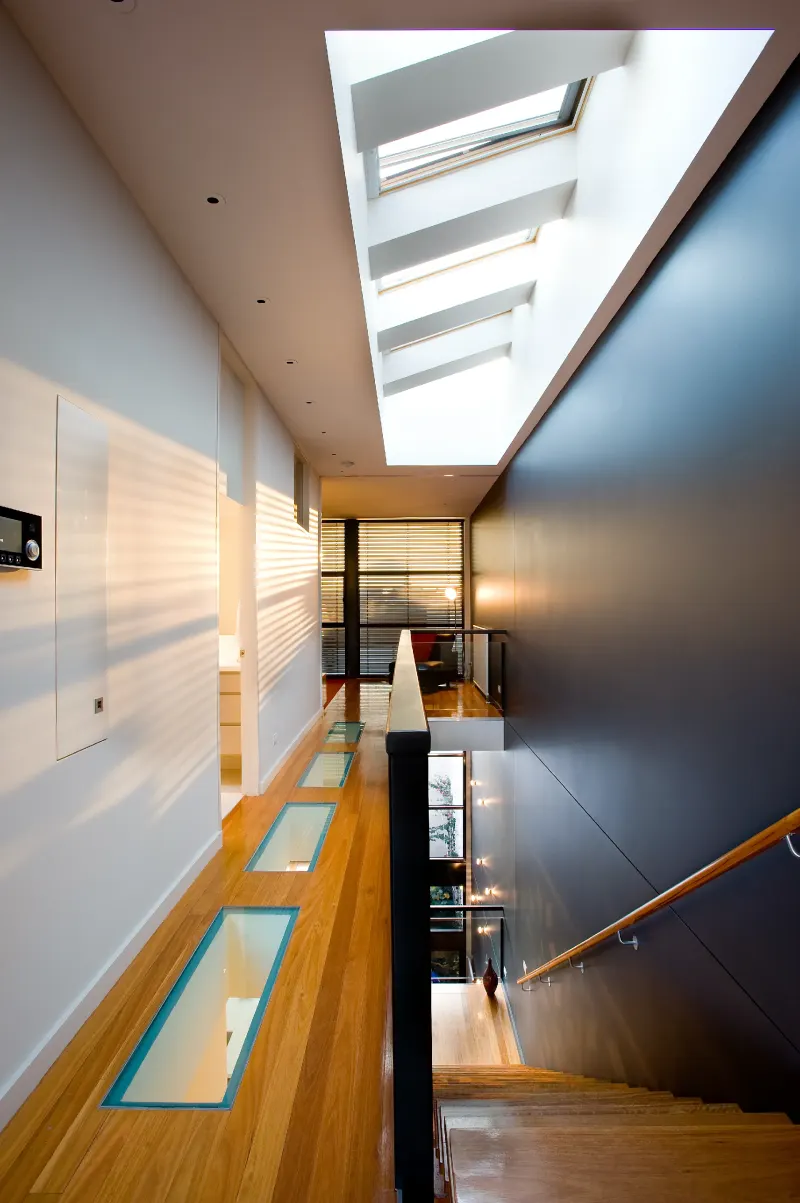 Residential stair and gallery landing lit by a run of skylights above timber floors