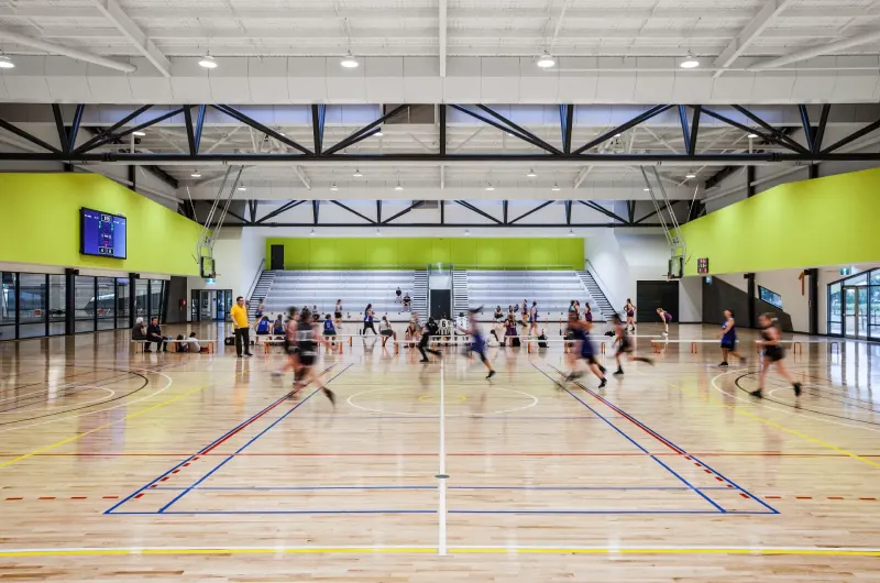 Indoor multi-sport court with timber floor, green walls and players mid-game