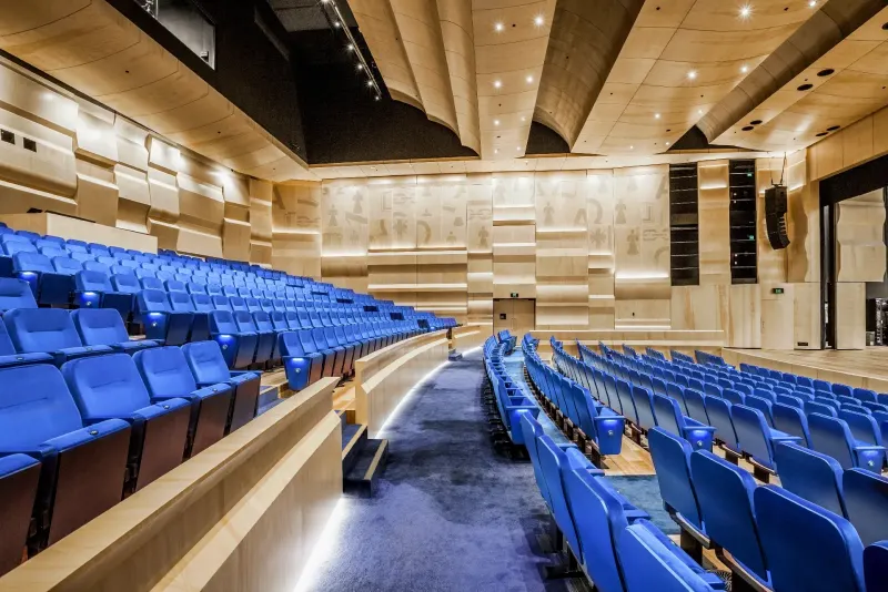 Auditorium with tiered blue seating and faceted timber acoustic wall panels