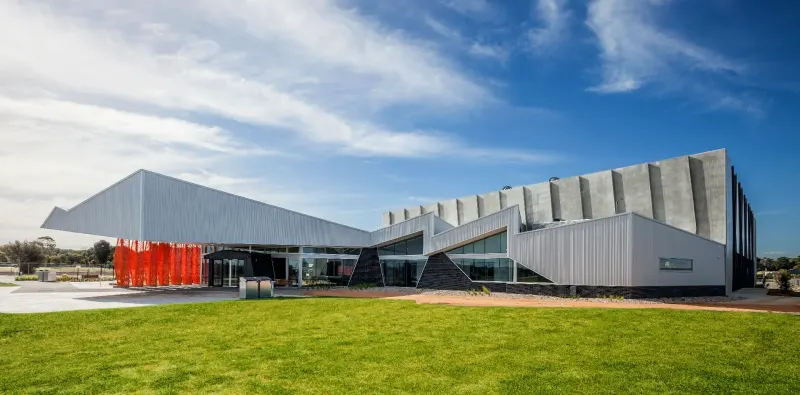 Faceted metal-clad civic centre with a red sculpture on the lawn beneath a wide sky